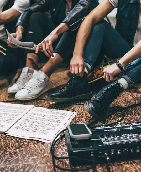 Repetition of rock music band. Cropped image of guitar players and drummer are sitting on the floor at rehearsal base with notes.